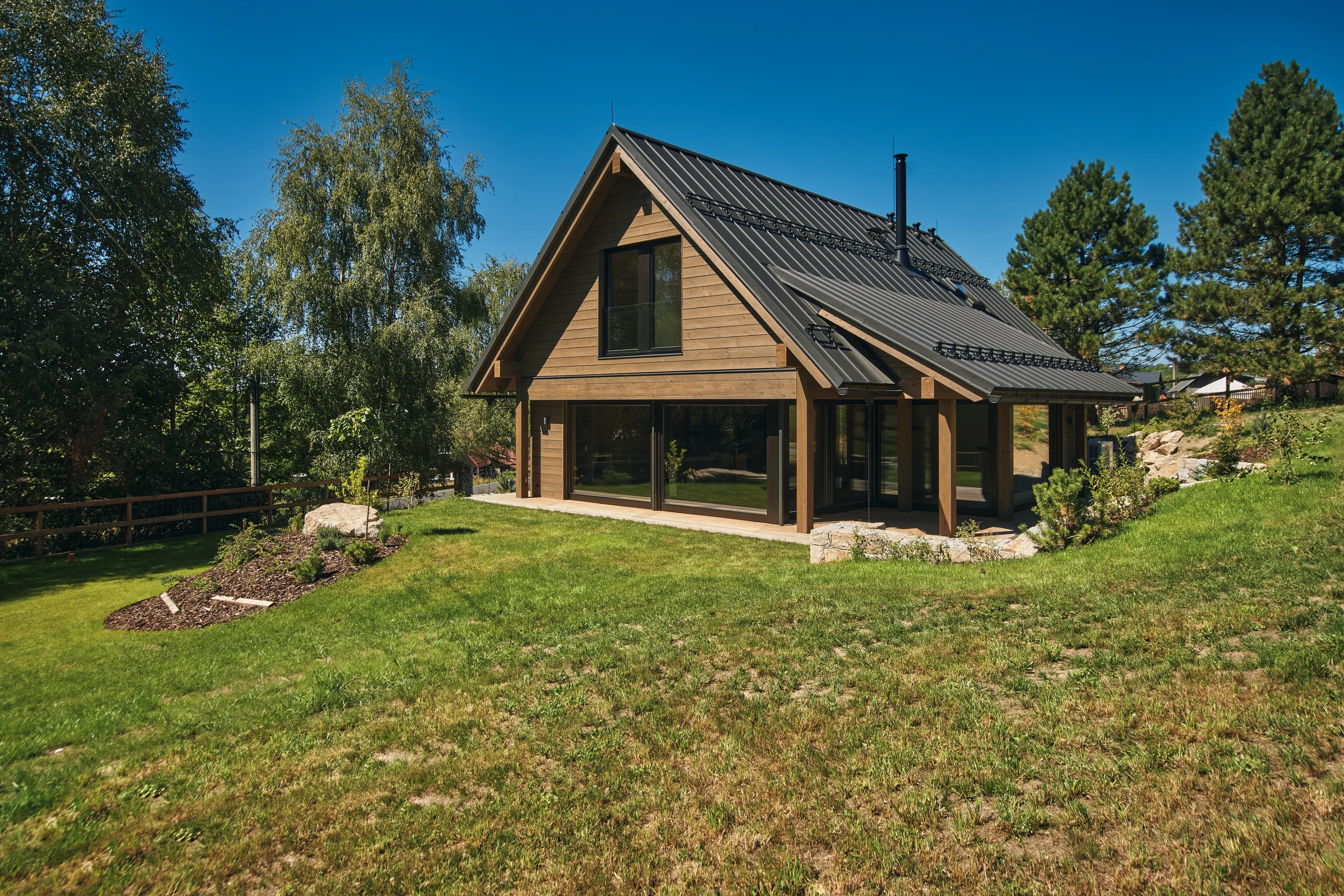 Dokončený dřevěný chalet s velkým prosklením, terasou a zahradou